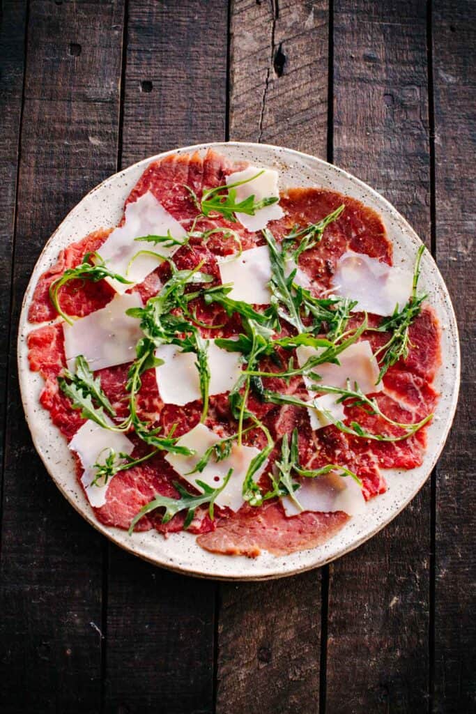 A plate of carpaccio of beef on a wooden table.