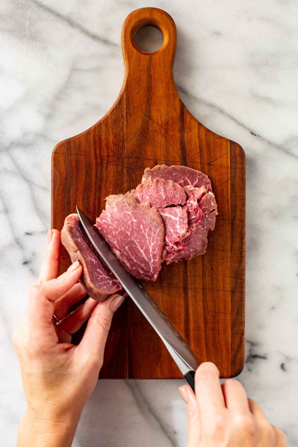 Thinly slicing beef tenderloin with a knife.