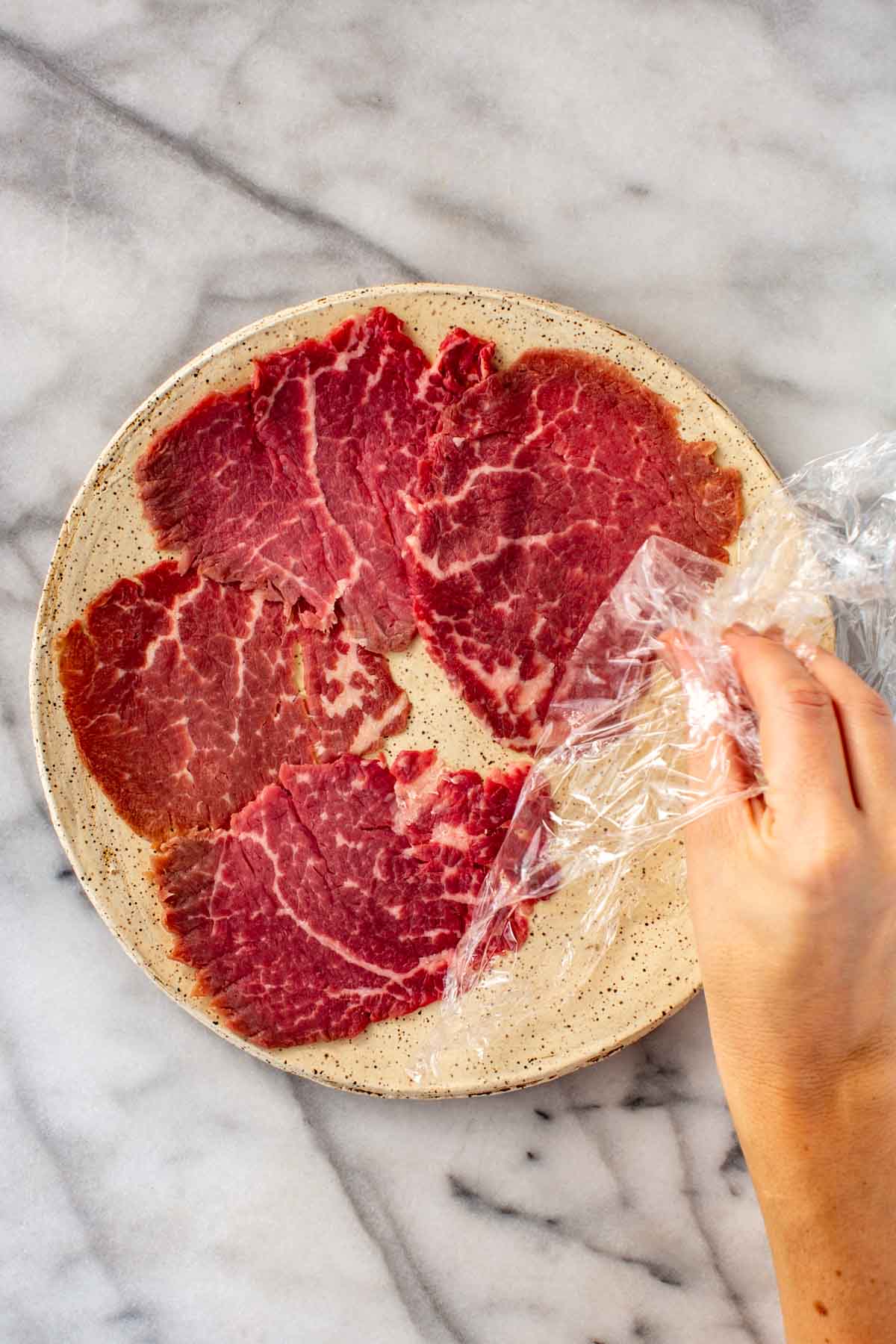 Removing plastic wrap from slices of beef carpaccio.