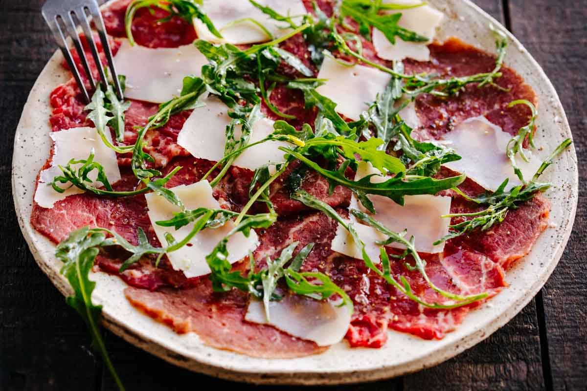 A plate of thinly sliced beef dressed with parmesan and arugula.