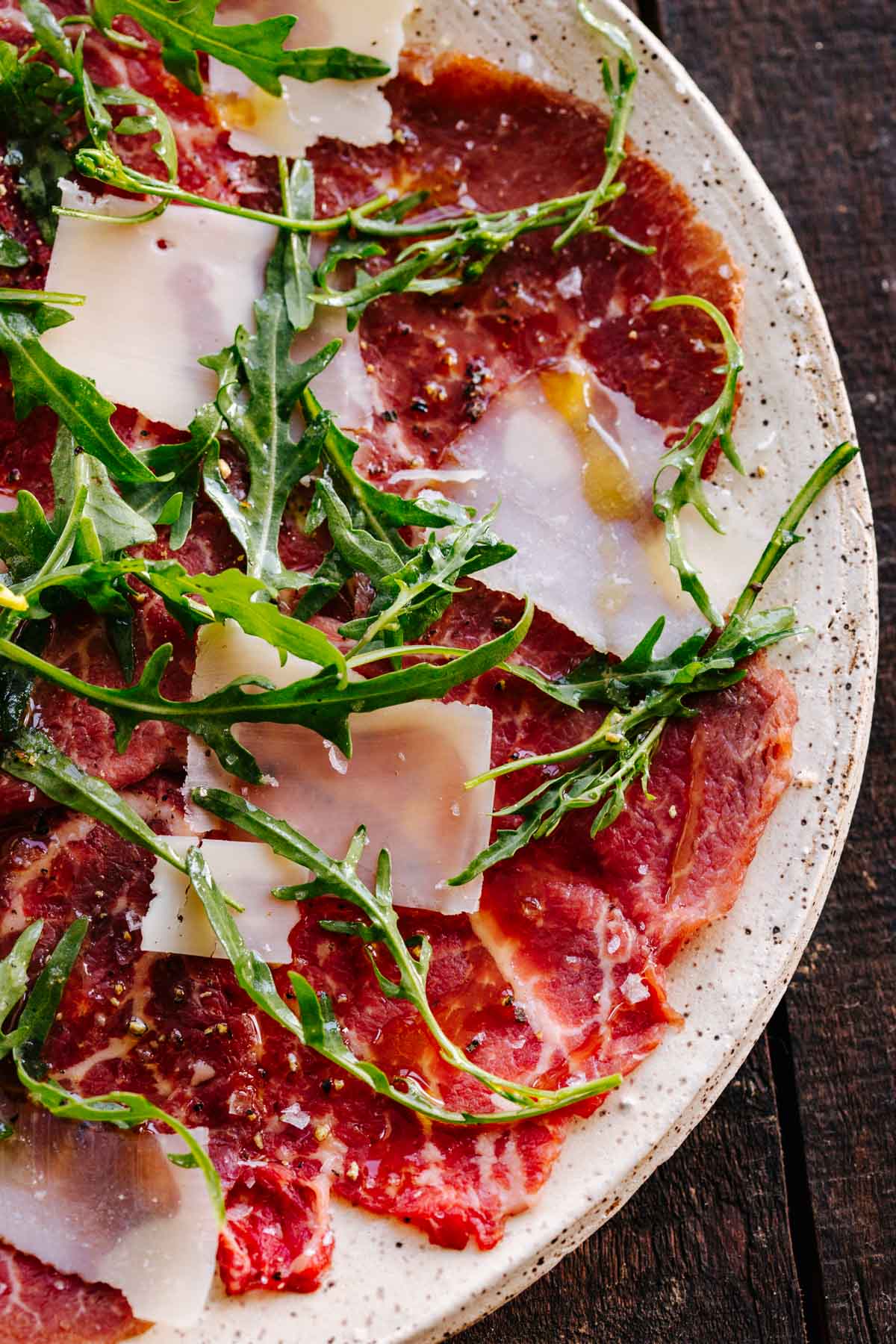 A plate of beef carpaccio with arugula and parmesan.