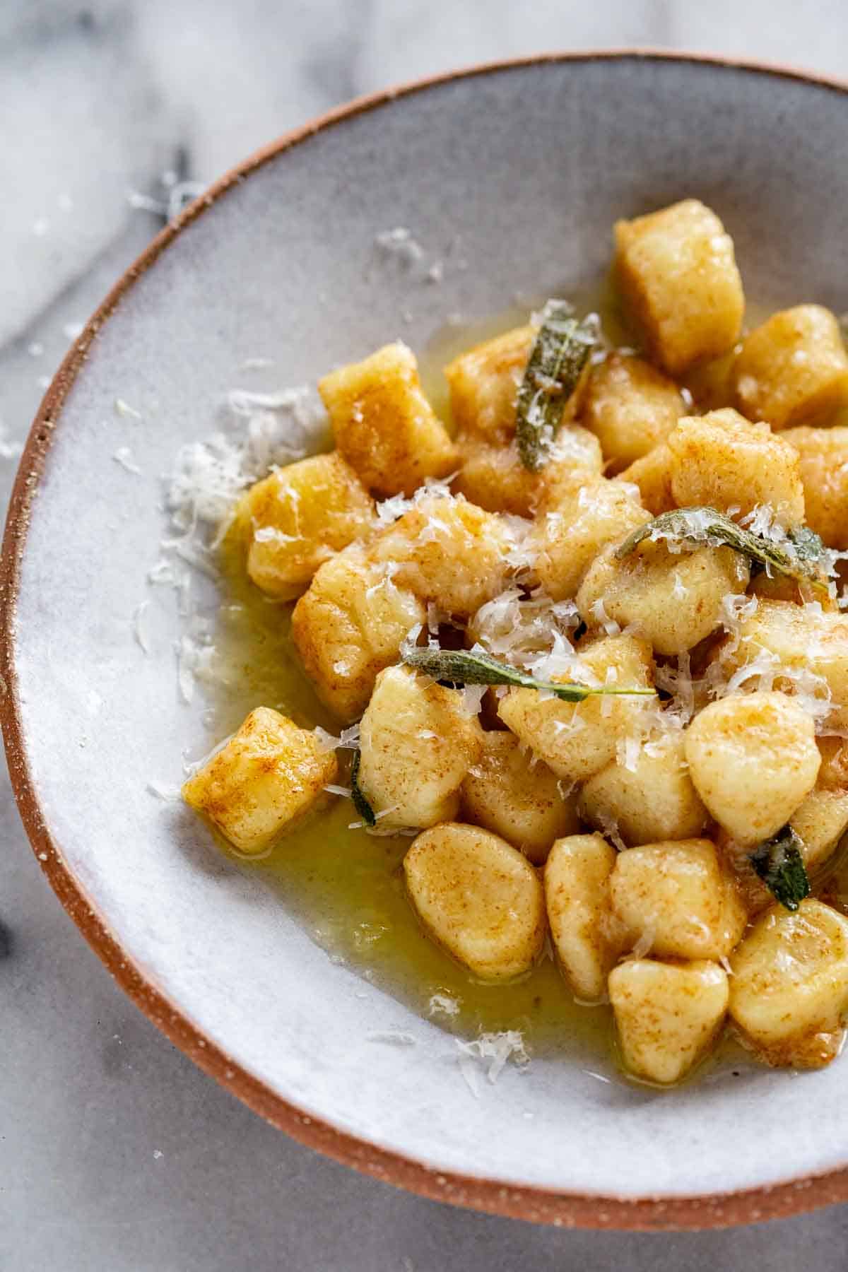 A ceramic plate with potato gnocchi, butter and cheese. 