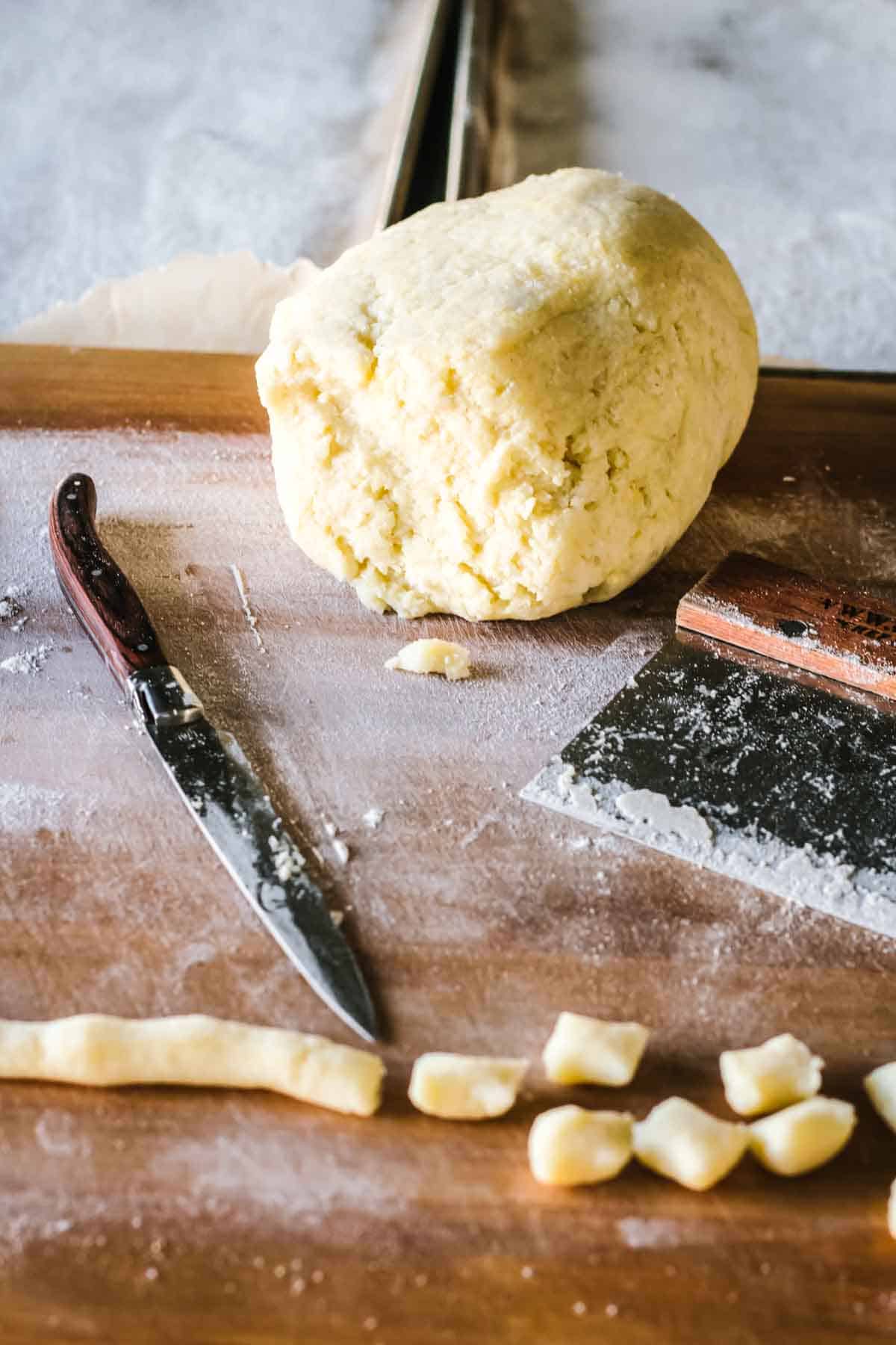 A ball of potato gnocchi dough along with a rope of dough being cut into pieces.