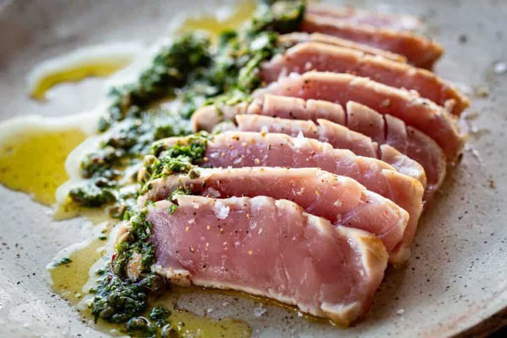 Rare seared tuna sliced on a plate with an herb sauce.