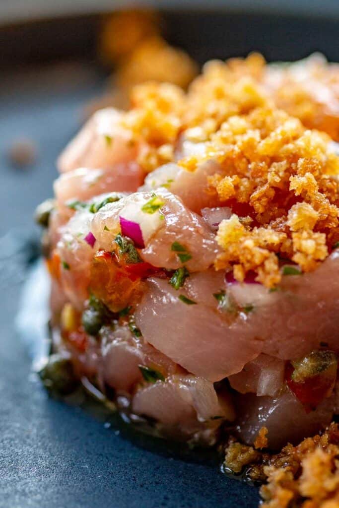 Close up of fresh raw ahi tuna tartare with capers, tomatoes, red onion and breadcrumbs on top.