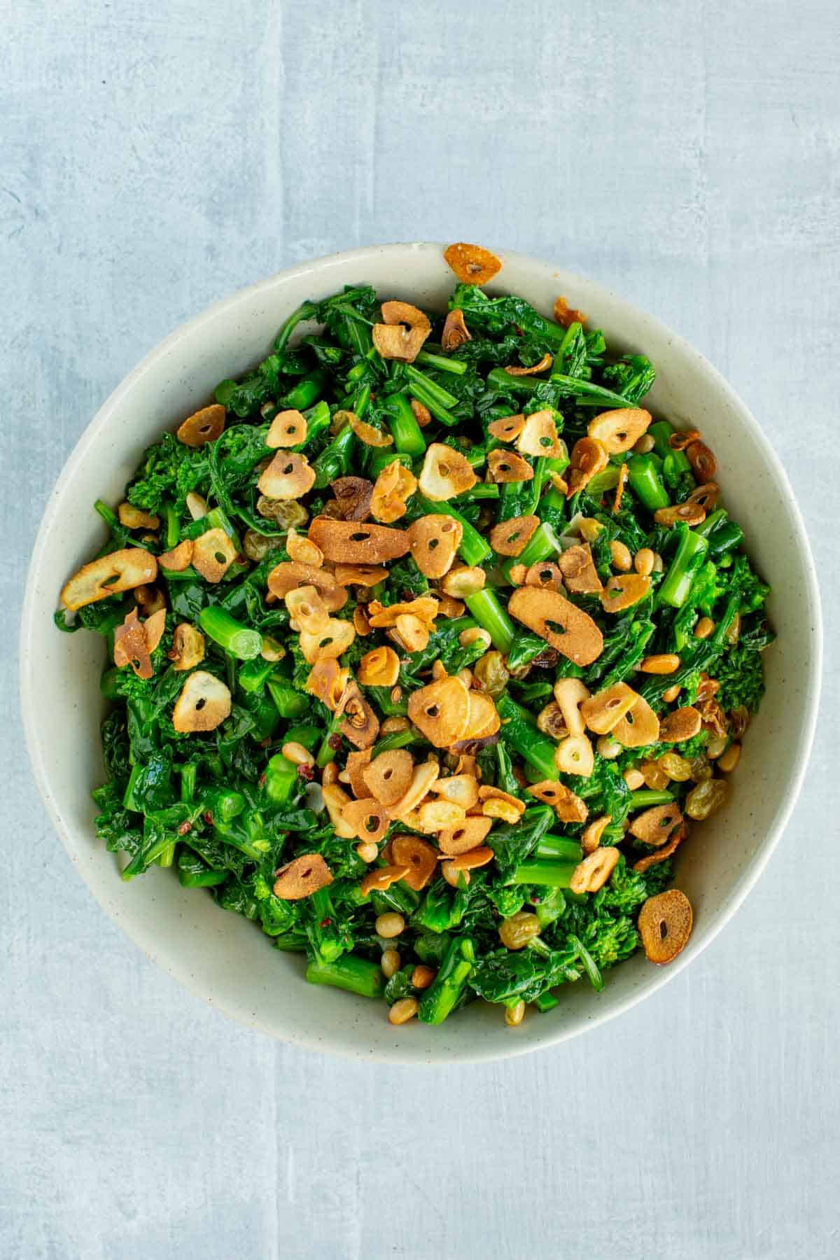 A bowl of sauteed rapini with crispy garlic slices on top.