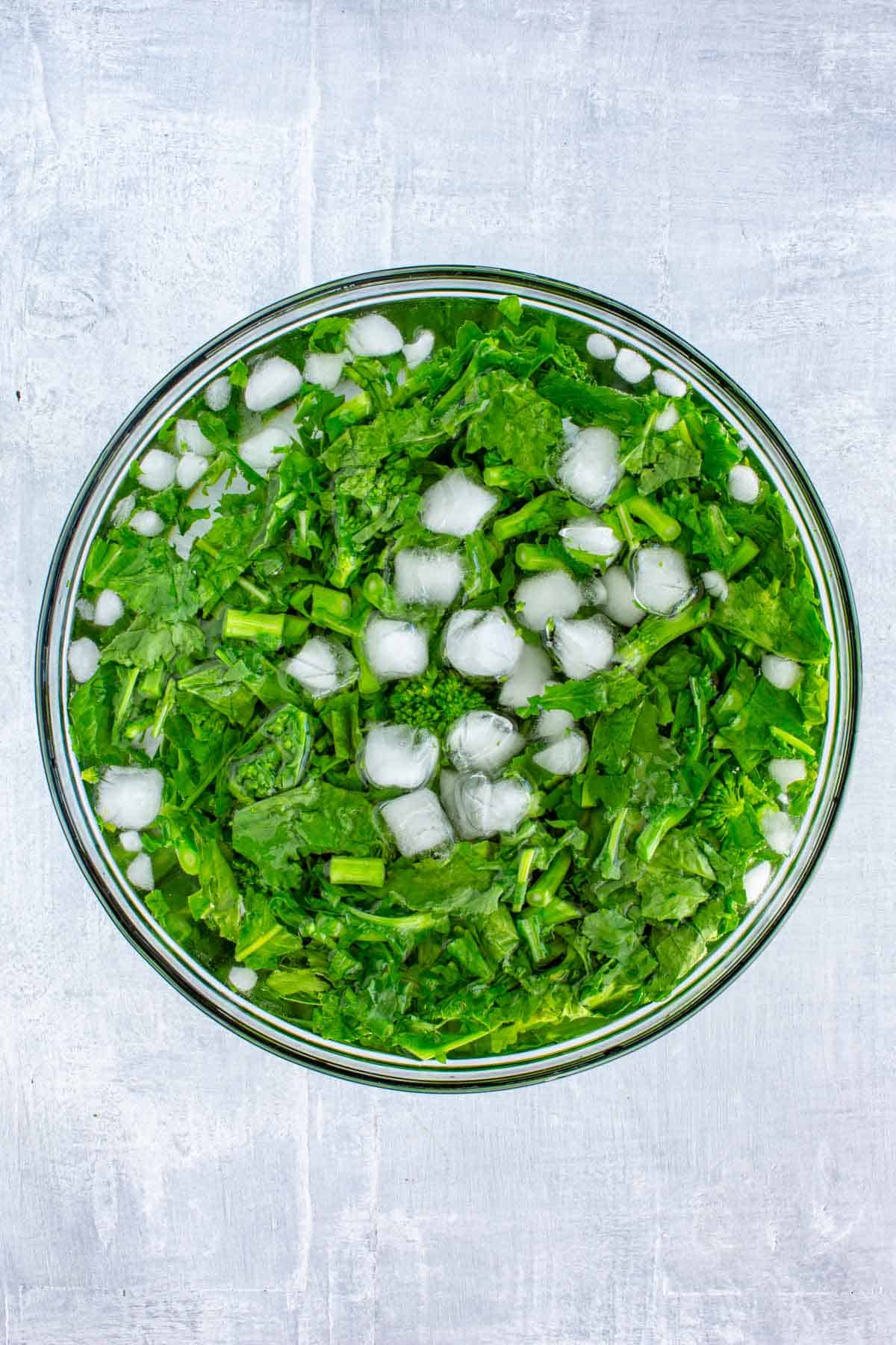 A bowl of ice water and blanched green vegetables.