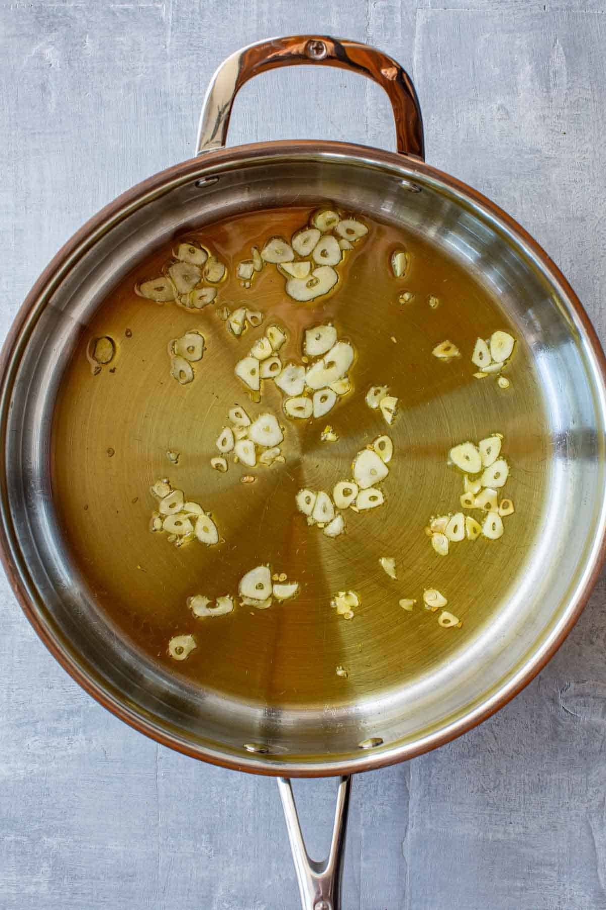 A saute pan with olive oil and thinly sliced garlic.