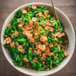 A bowl of broccoli rabe with pine nuts, raisins and crispy garlic.