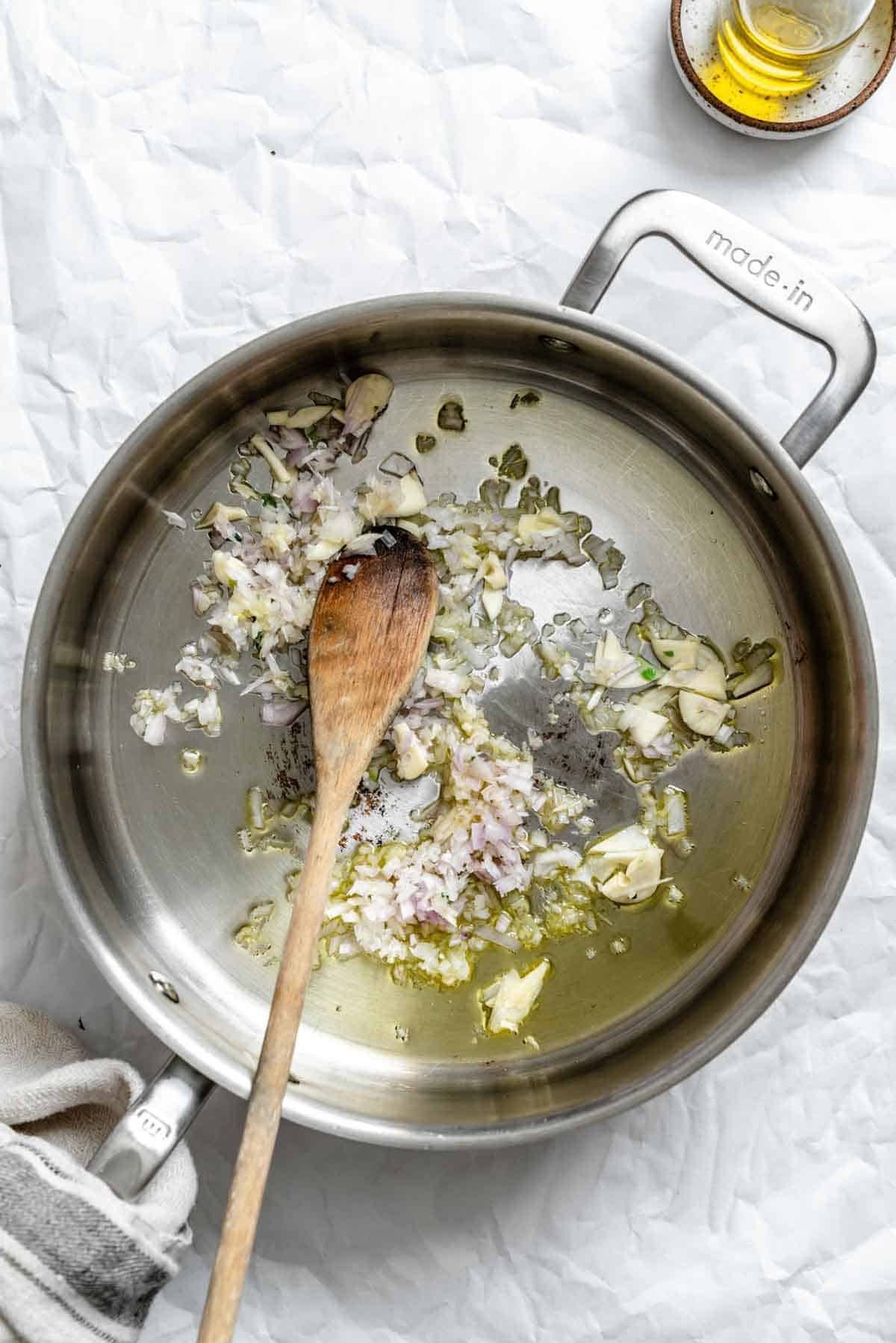 Stirring garlic and shallots in olive oil in a saute pan.