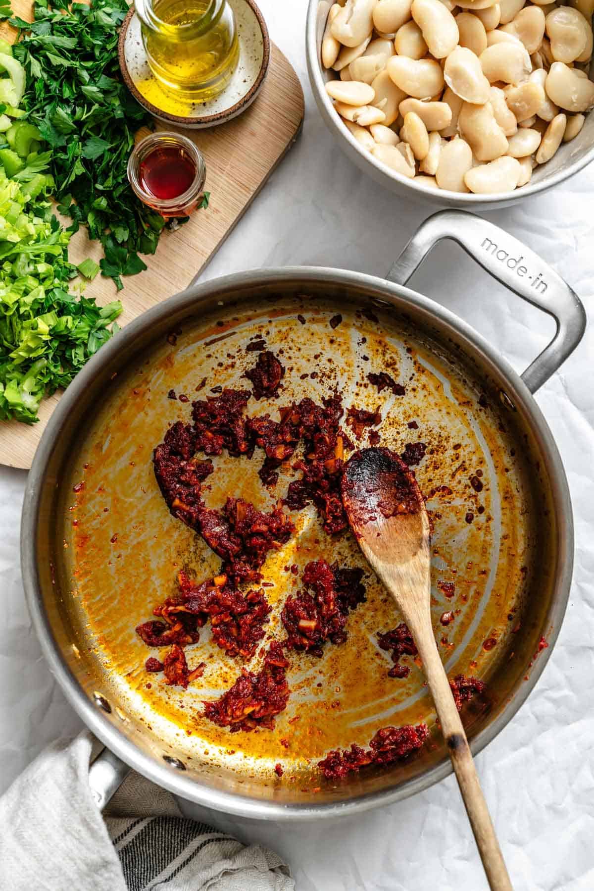 Stirring browned tomato paste in a pan with a wooden spoon.