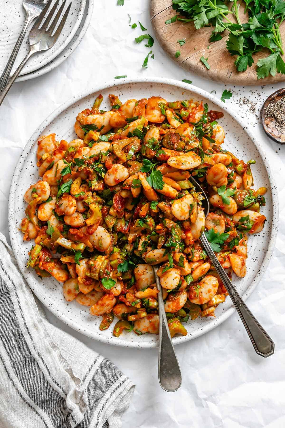 Spanish style gigante bean salad with silverware on a white plate.