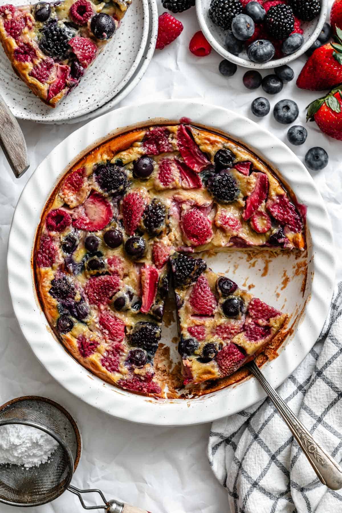 Overhead view of a slice of berry clafoutis on a serving utensil, showing the creamy texture and embedded berries.
