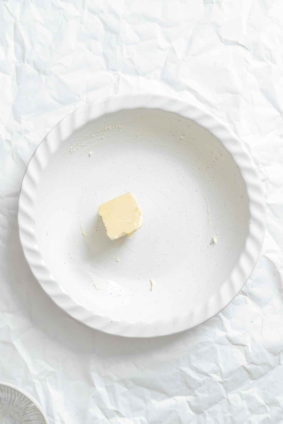 Small pat of butter greasing a white ceramic plate.