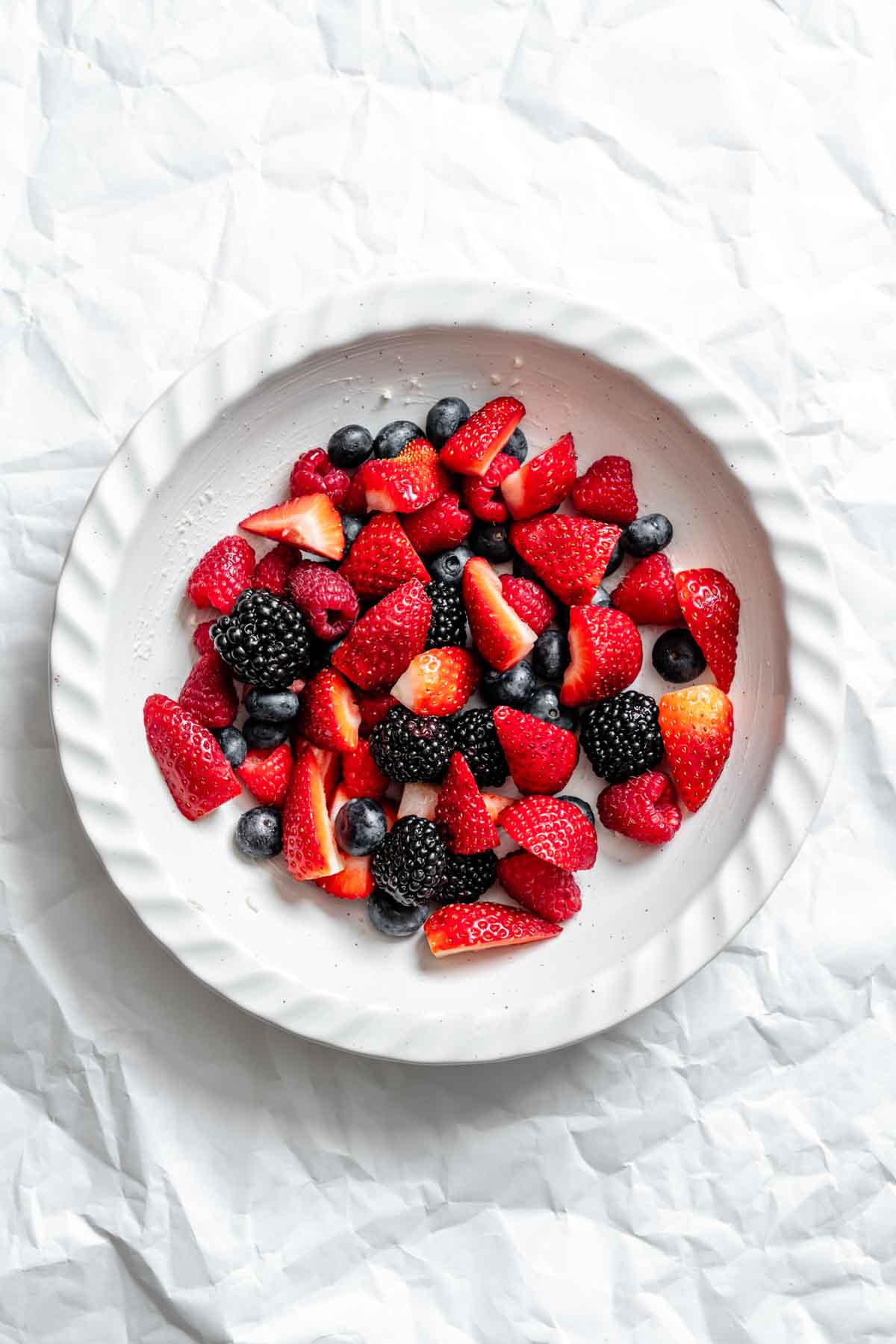 Fresh mixed berries including strawberries, blackberries, blueberries, and raspberries in a white ceramic bowl.