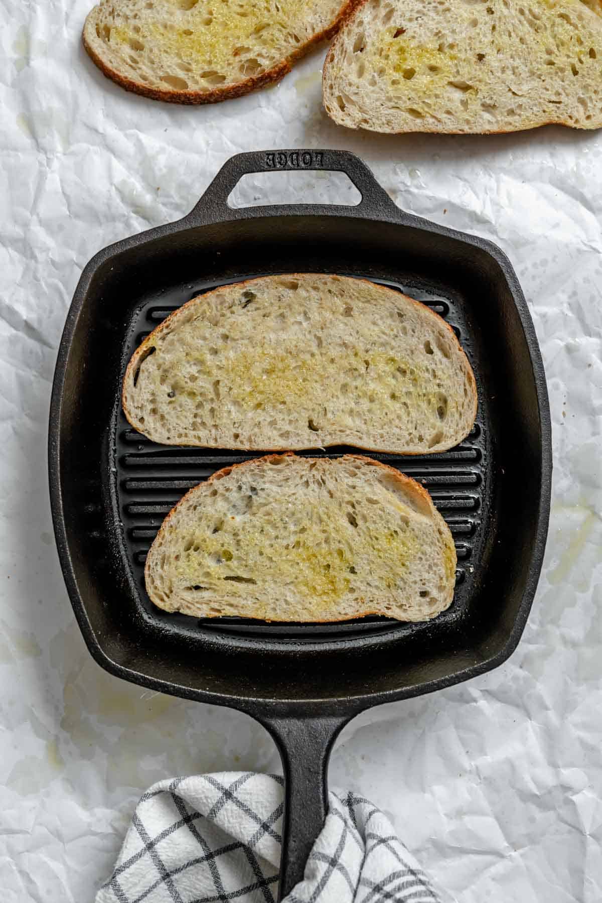 Cast iron grill pan with bread slices being toasted on parchment paper.