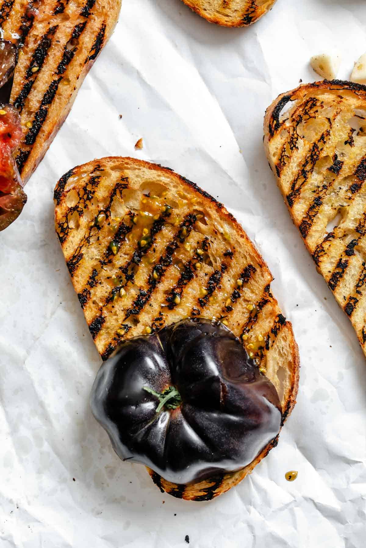 Close-up of grilled bread being rubbed with a purple tomato.