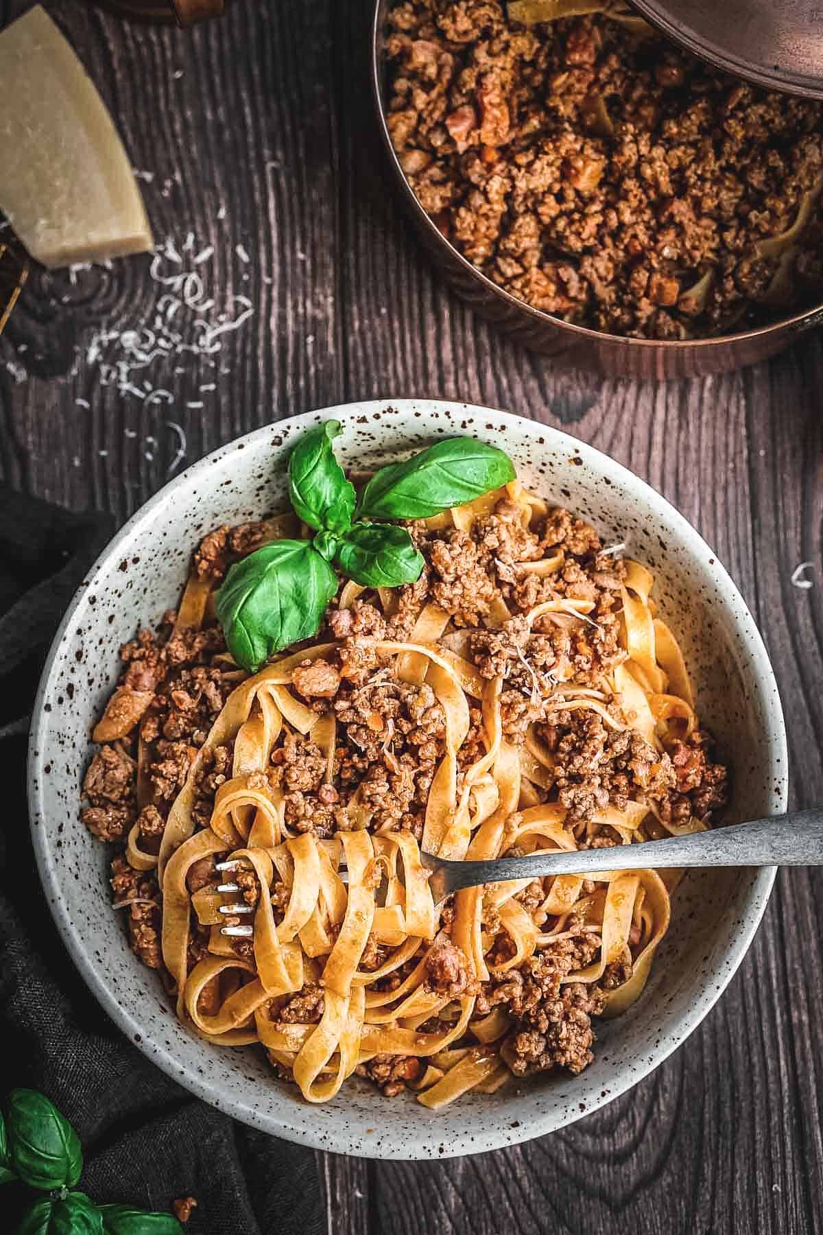 A bowl of pasta with ragu alla Bolognese with a fork.