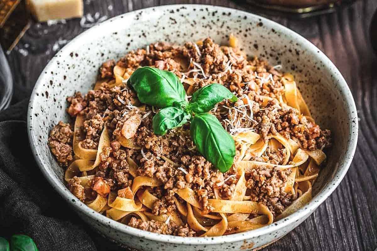 A bowl of tagliatelle pasta with ragu alla Bolognese garnished with a basil sprig.