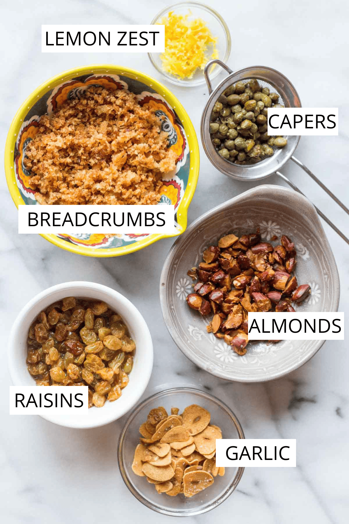 Toppings arranged in separate bowls, including breadcrumbs, capers, golden raisins, toasted almonds, and lemon zest.