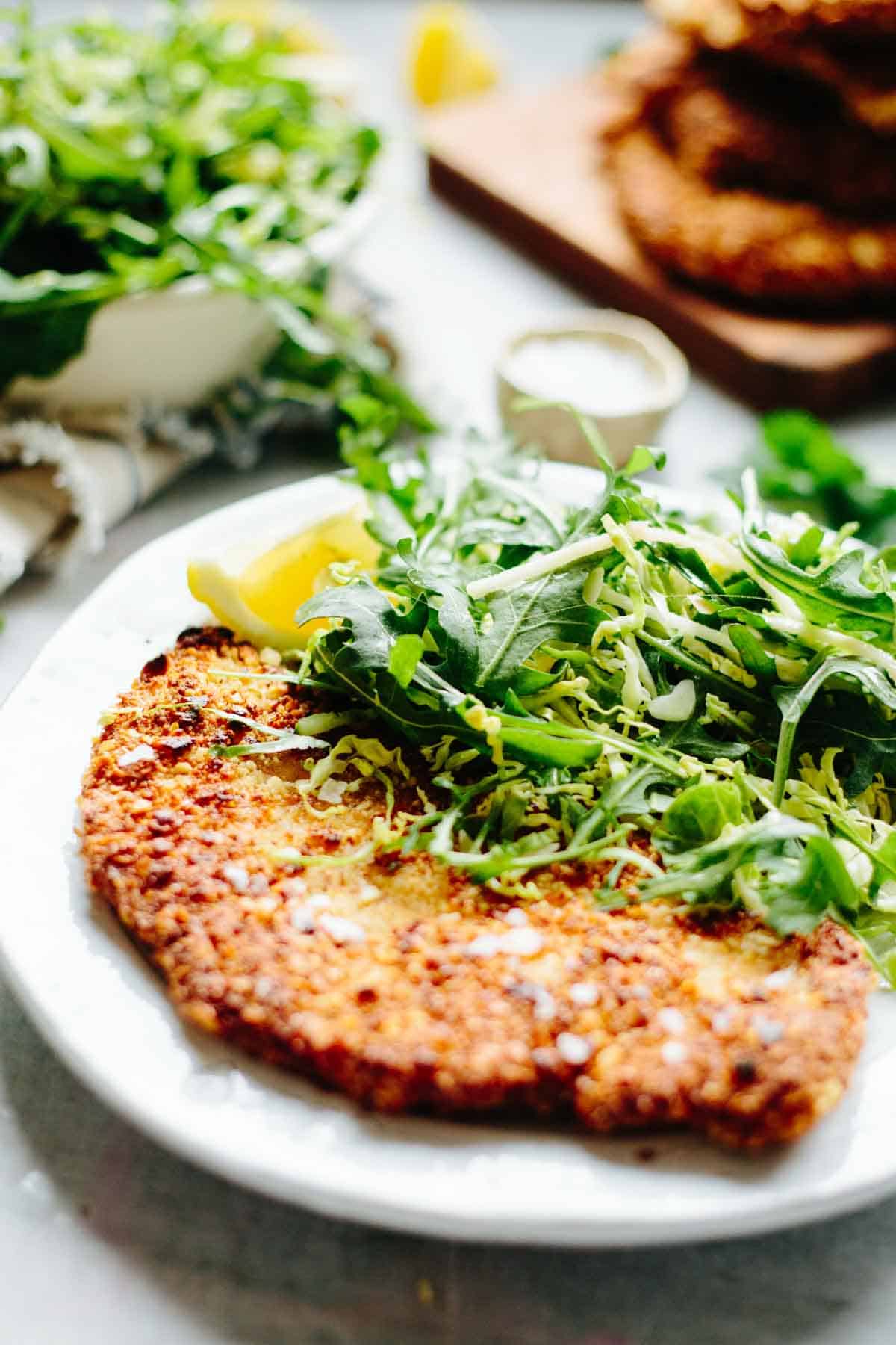 Close-up of a partially cut almond crusted chicken cutlet with fork, showing the tender meat inside and crispy coating, served with fresh greens.