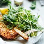 Side view of almond crusted chicken cutlet on a white plate with green salad, highlighting the crispy exterior and juicy interior.