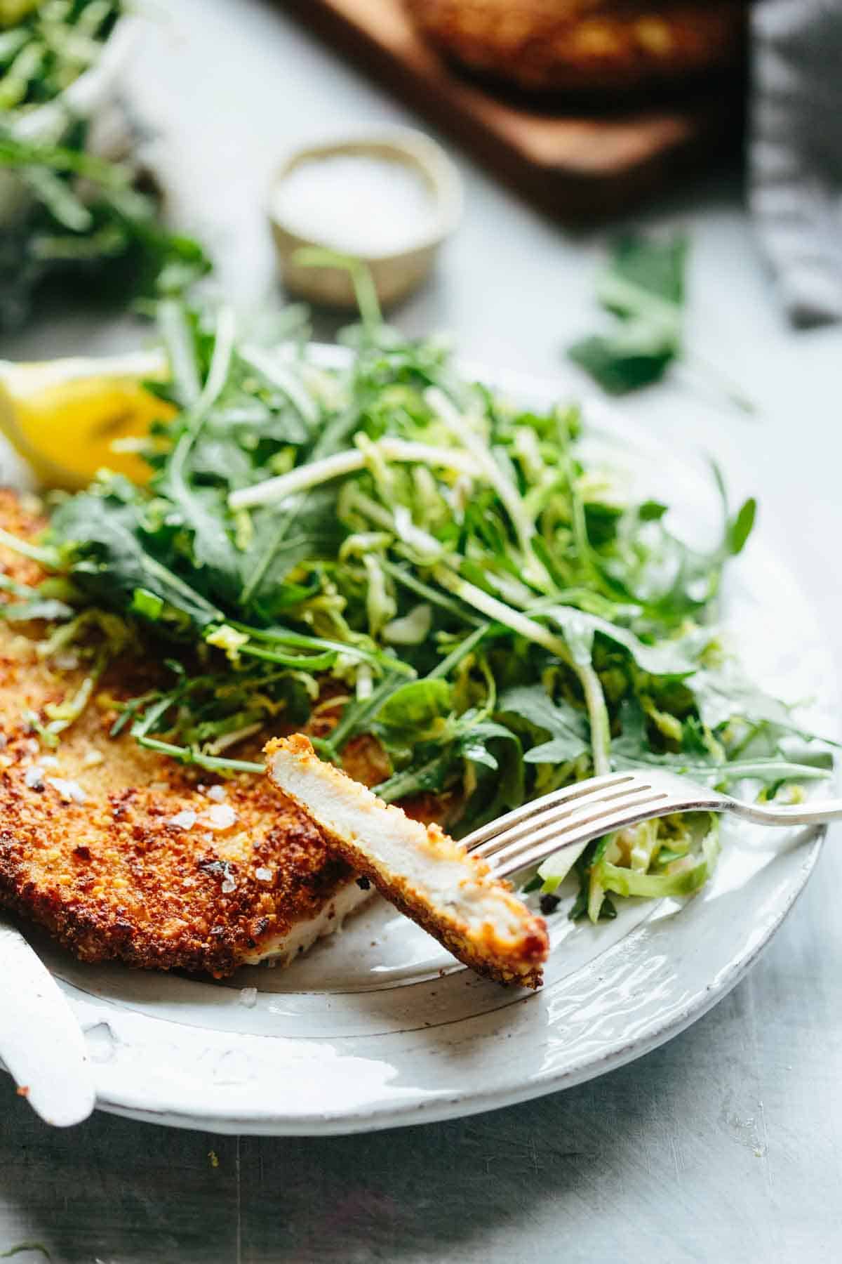 Side view of almond crusted chicken cutlet on a white plate with green salad, highlighting the crispy exterior and juicy interior.