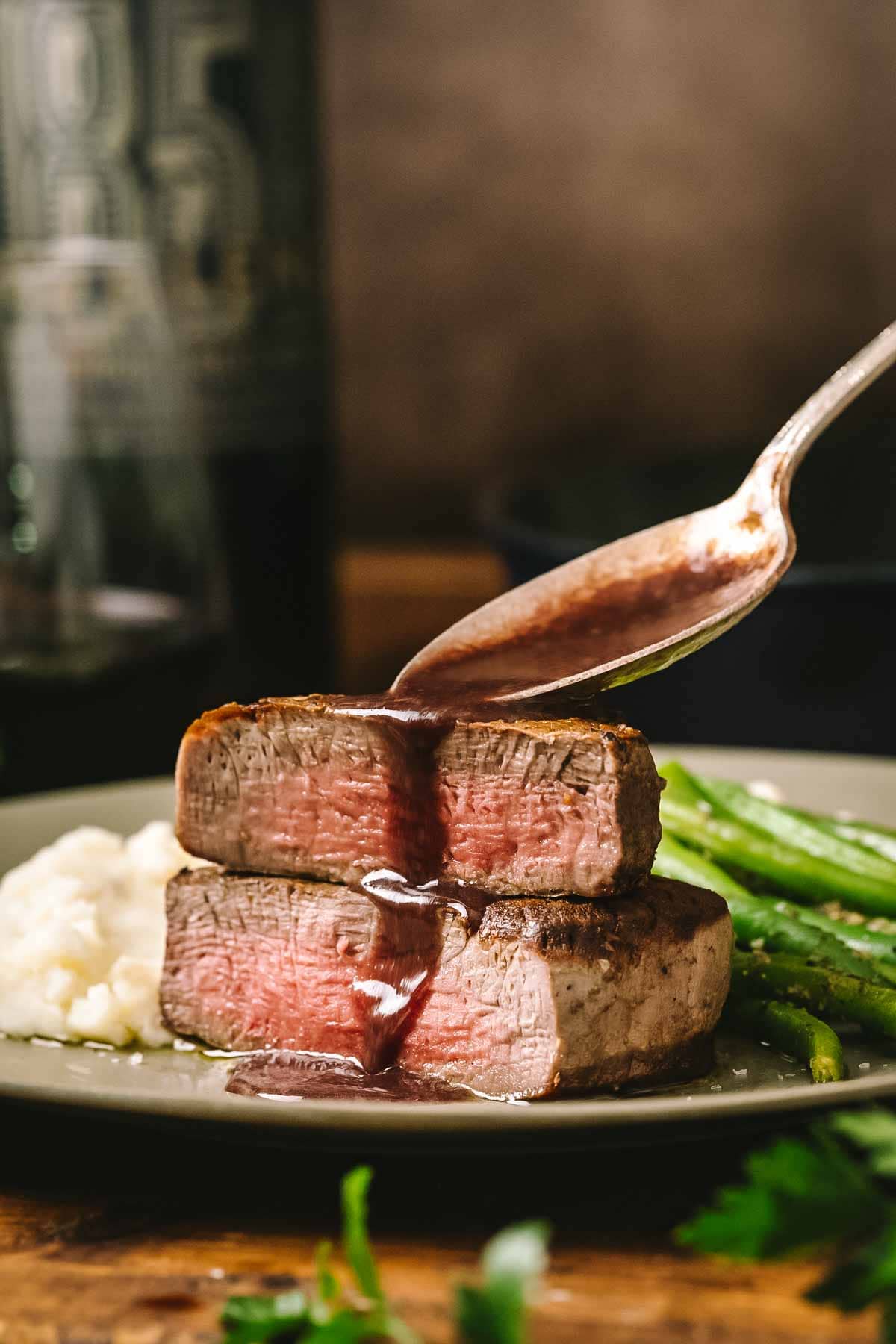 A close-up of a perfectly cooked medium-rare steak on a plate with bordelaise sauce being spooned over it.