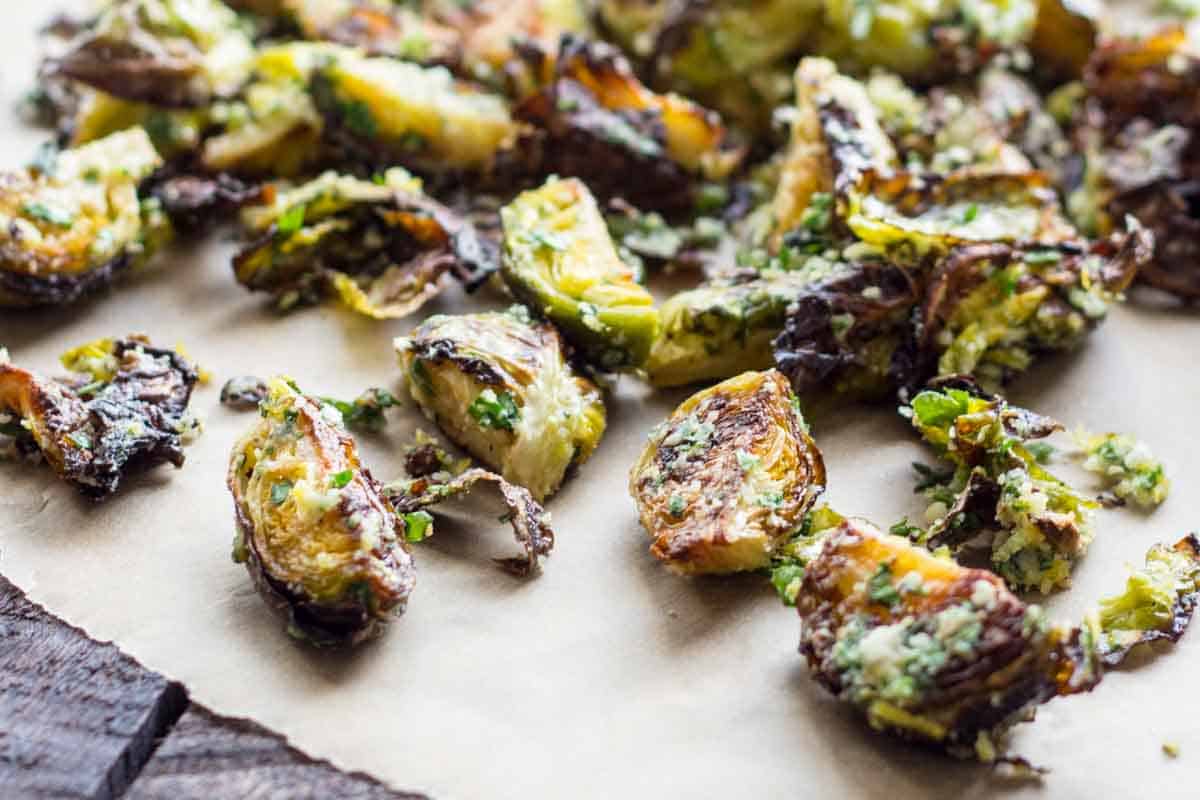 A closer view of roasted Brussels sprouts on parchment paper, showing their golden-brown exterior. The vegetable pieces are tossed with what appears to be finely grated Pecorino cheese and fresh herbs, giving them a textured coating.