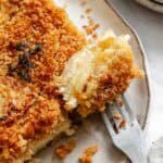 An extreme close-up of a forkful of the parsnip and celery root gratin, showcasing the tender vegetable layers and creamy sauce, with the remaining portion visible on a rustic ceramic plate.
