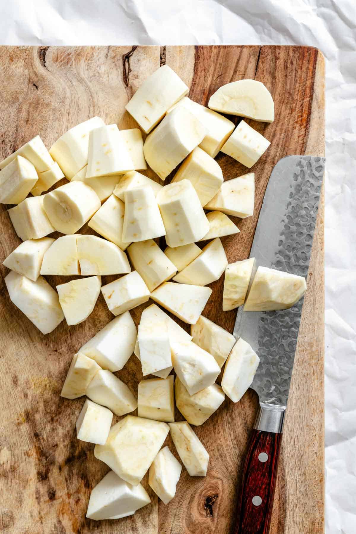 Diced parsnips on a wooden cutting board with a chef's knife. The white, cream-colored root vegetable is cut into uniform chunks ready for cooking.
