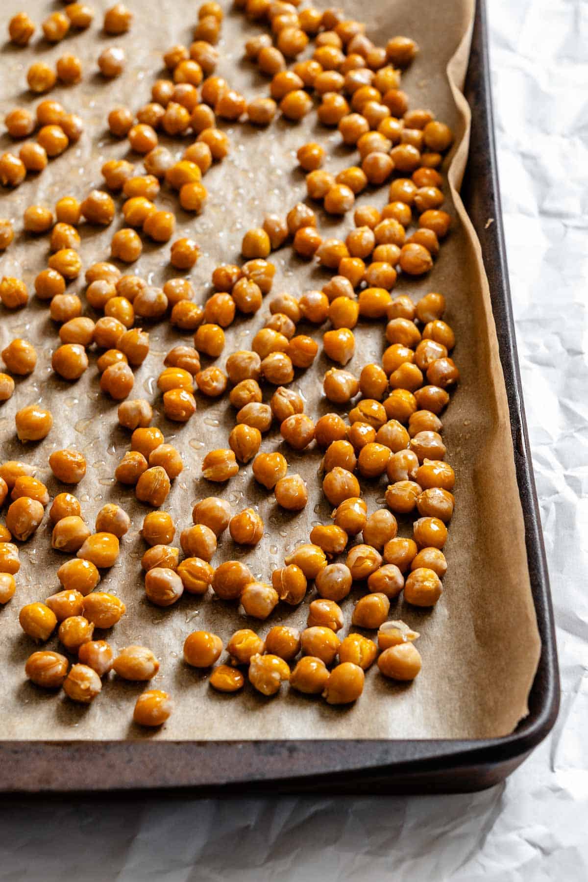 Seasoned chickpeas spread out on a baking sheet lined with parchment paper, ready to be roasted until crispy.