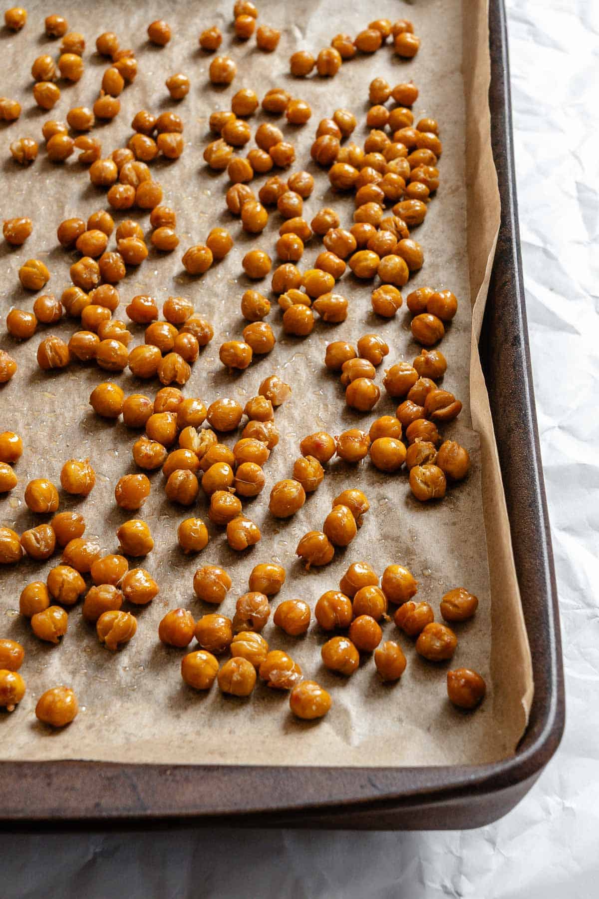Close-up view of seasoned chickpeas spread evenly on parchment-lined baking sheet before roasting.