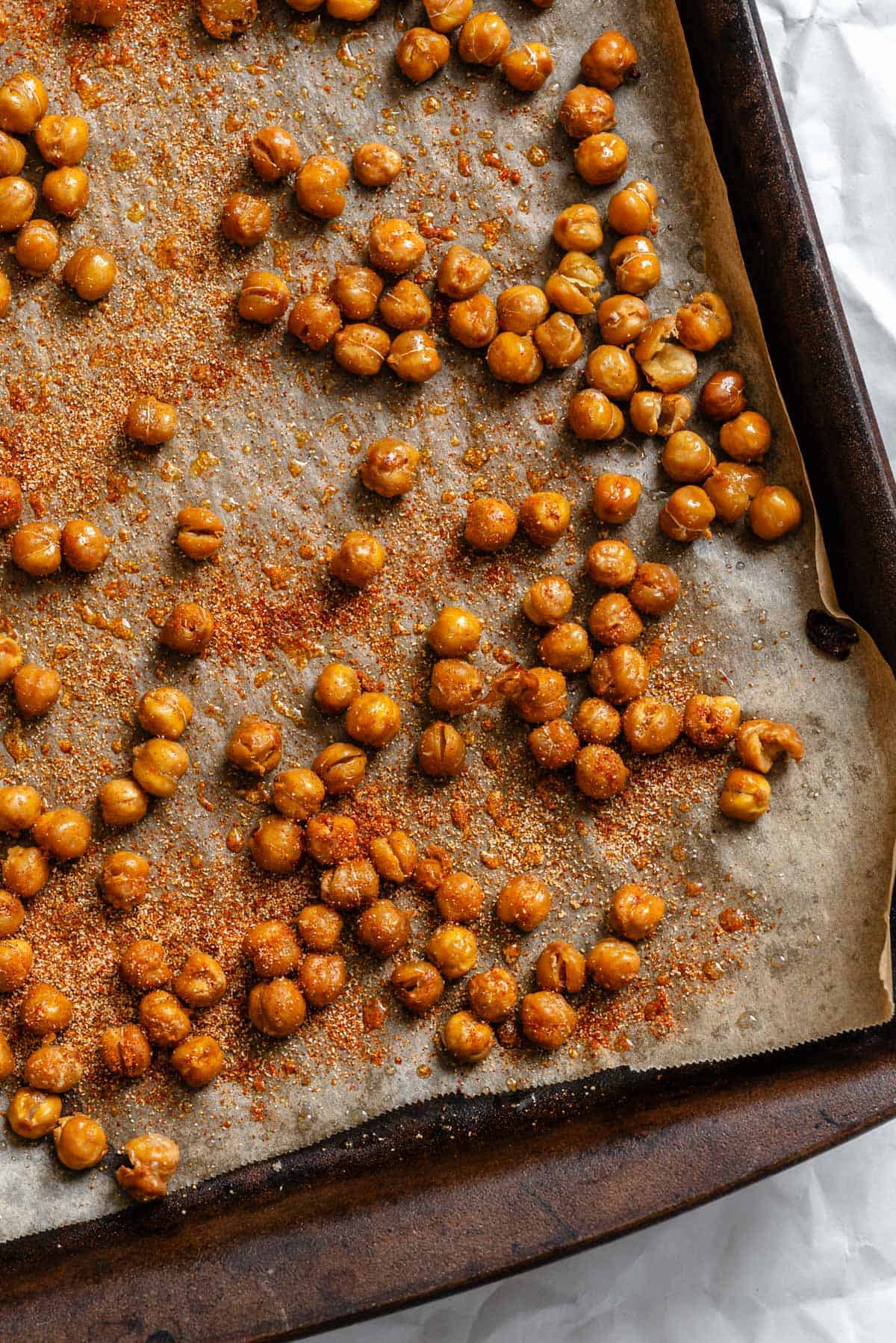 Top-down view of seasoned chickpeas on a baking sheet showing reddish spice coating applied to the chickpeas.