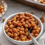 Close-up of a white speckled bowl filled with crispy roasted chickpeas with a small silver spoon inserted among the chickpeas.