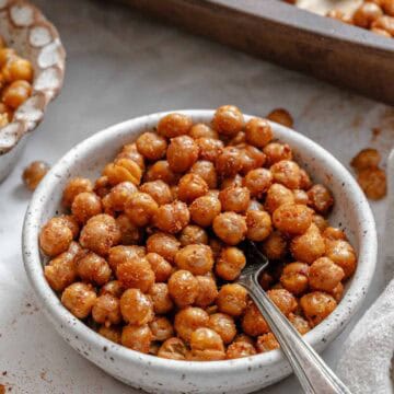 Close-up of a white speckled bowl filled with crispy roasted chickpeas with a small silver spoon inserted among the chickpeas.