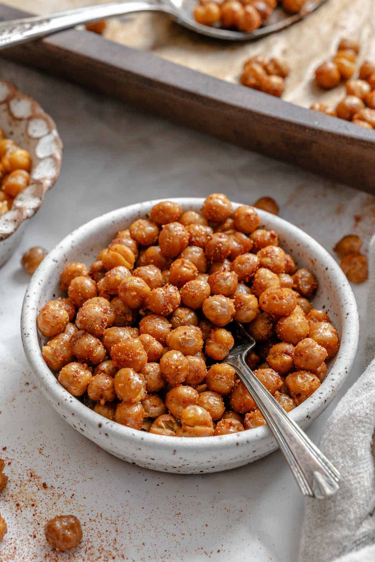 Close-up of a white speckled bowl filled with crispy roasted chickpeas with a small silver spoon inserted among the chickpeas.