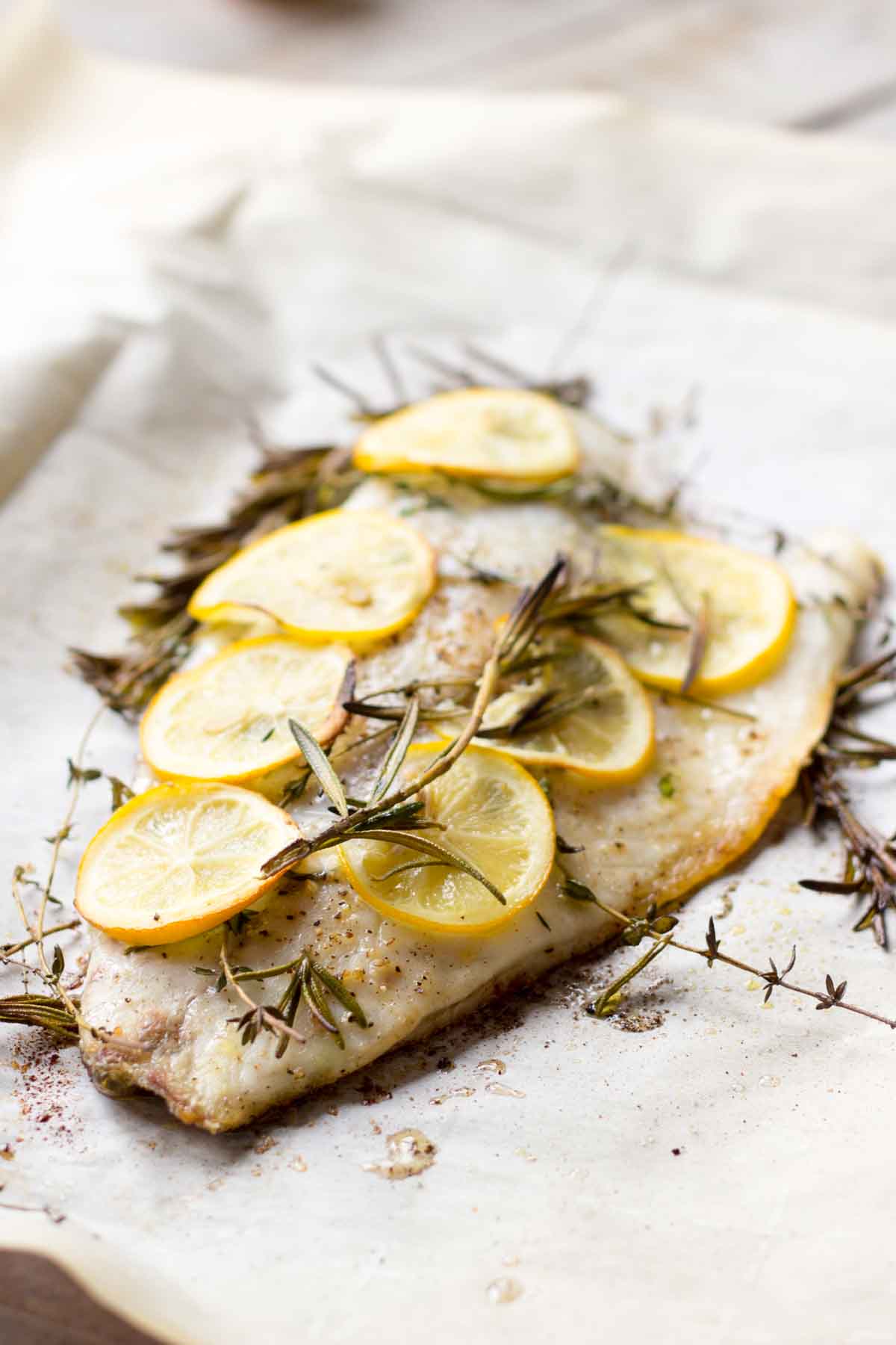 White fish fillet on parchment paper topped with thin lemon slices and fresh rosemary sprigs.