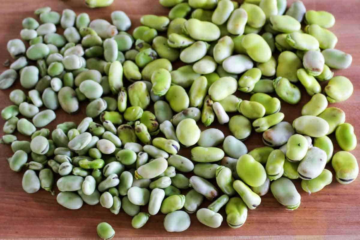 Pile of shelled fresh fava beans on a wooden surface, showing their pale green color and kidney-like shape after being removed from pods.
