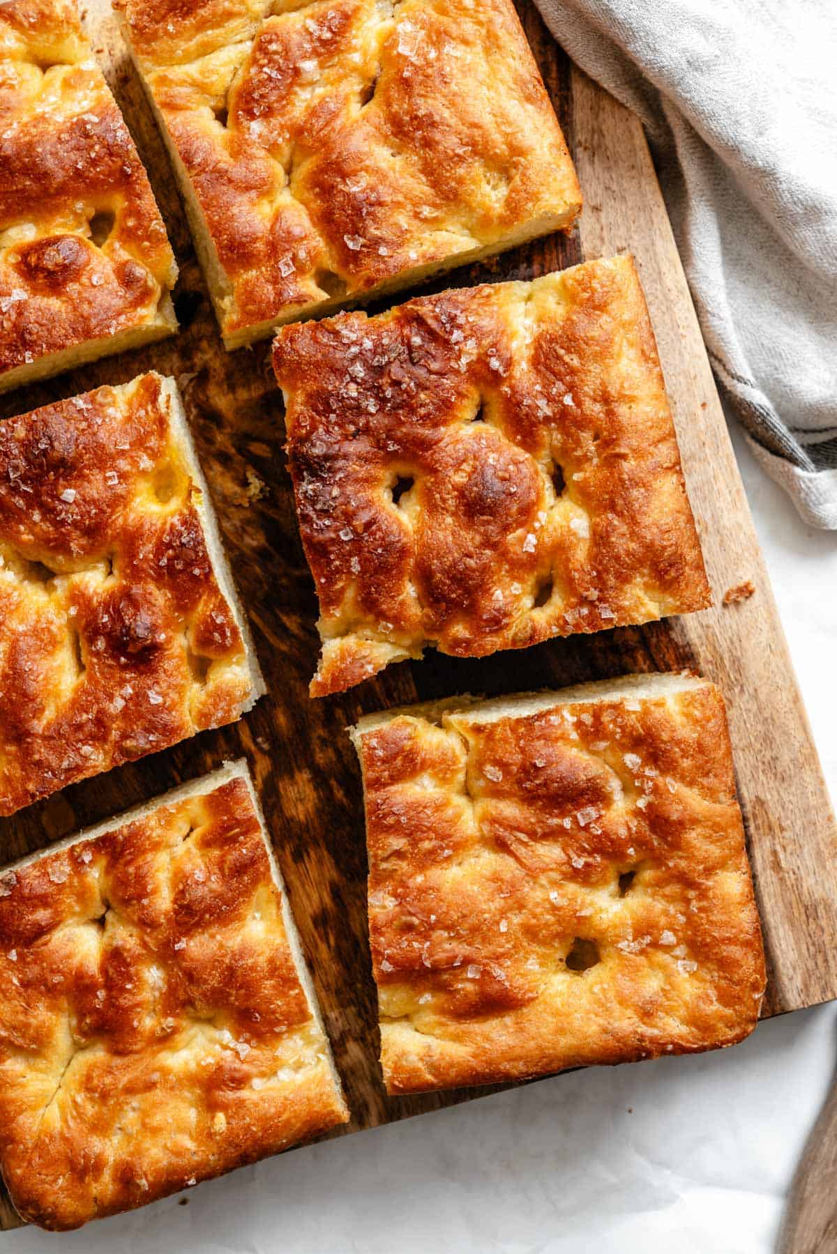 Overhead view of freshly baked golden-brown focaccia bread cut into square pieces on a wooden cutting board.