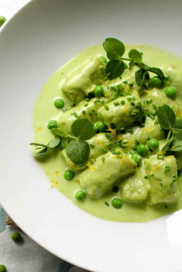 Macro view of tender spring pea gnocchi topped with fresh herbs and bright green peas in a silky sauce.