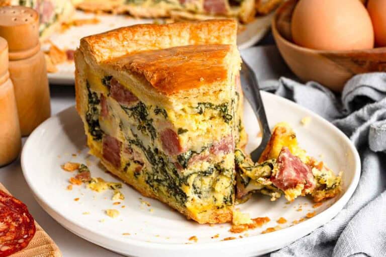 A slice of Italian Easter pie on a white plate showing the savory filling of cheese, ham and spinach inside a golden pastry crust.