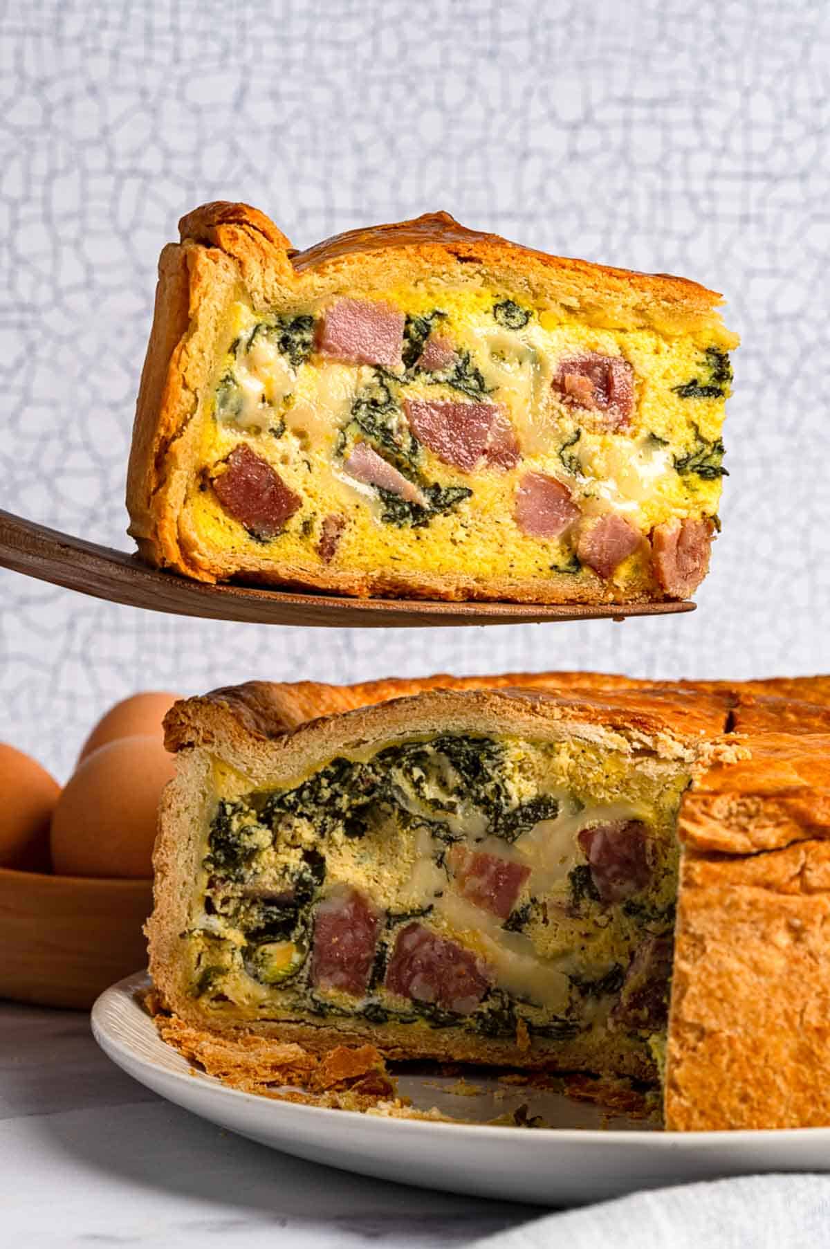 Close-up view of Italian Easter pie showing both a slice being lifted with a spatula and the cross-section of the pie revealing layers of meat, cheese and spinach in the filling.