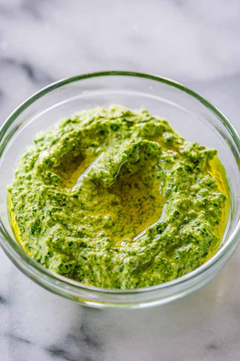 Glass bowl of finished spinach pesto with a pool of olive oil on top, showing the rich, vibrant green color and creamy texture.