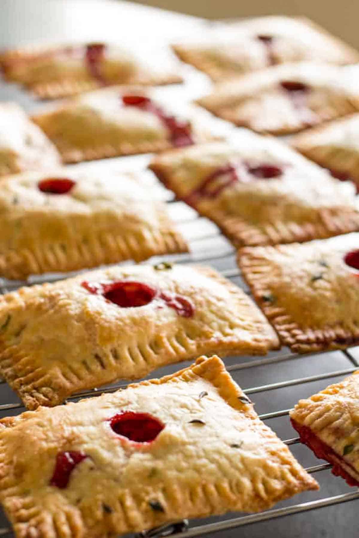 Finished pastries cooling on a wire rack. They're golden brown with crimped edges and small holes in the center where red filling is visible.