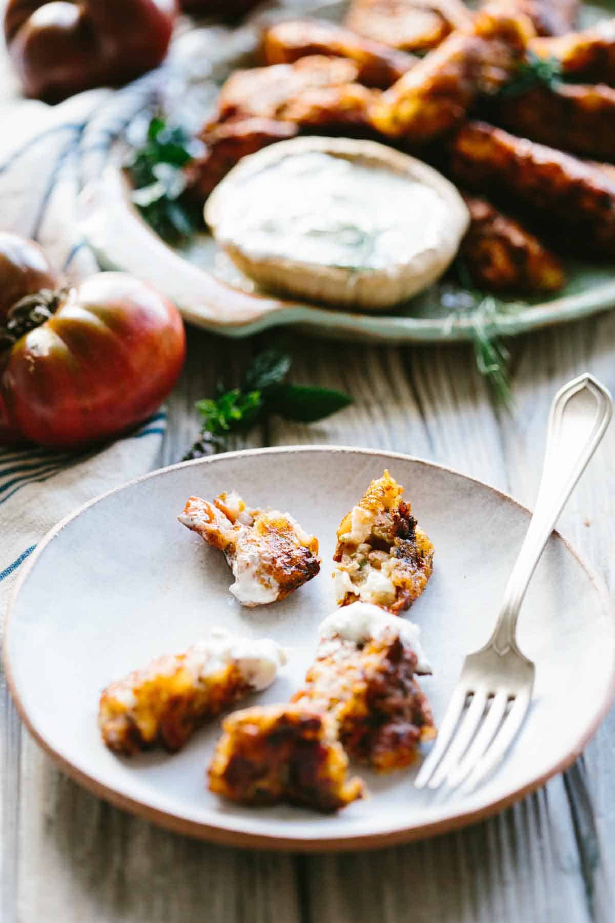 Bits of crispy tomato fritter rest on a ceramic plate, split open to reveal their tender, cheesy interior. A few smears of tzatziki remain, suggesting a meal thoroughly enjoyed.