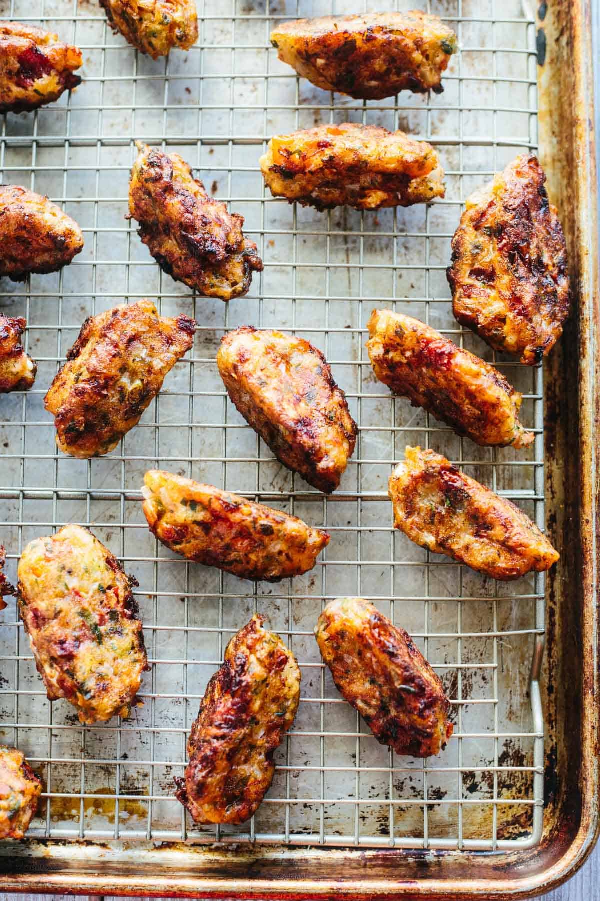 Freshly baked tomato fritters cool on a wire rack, their golden crusts evenly crisped and flecked with herbs. The clean, minimal backdrop highlights their homemade simplicity and texture.