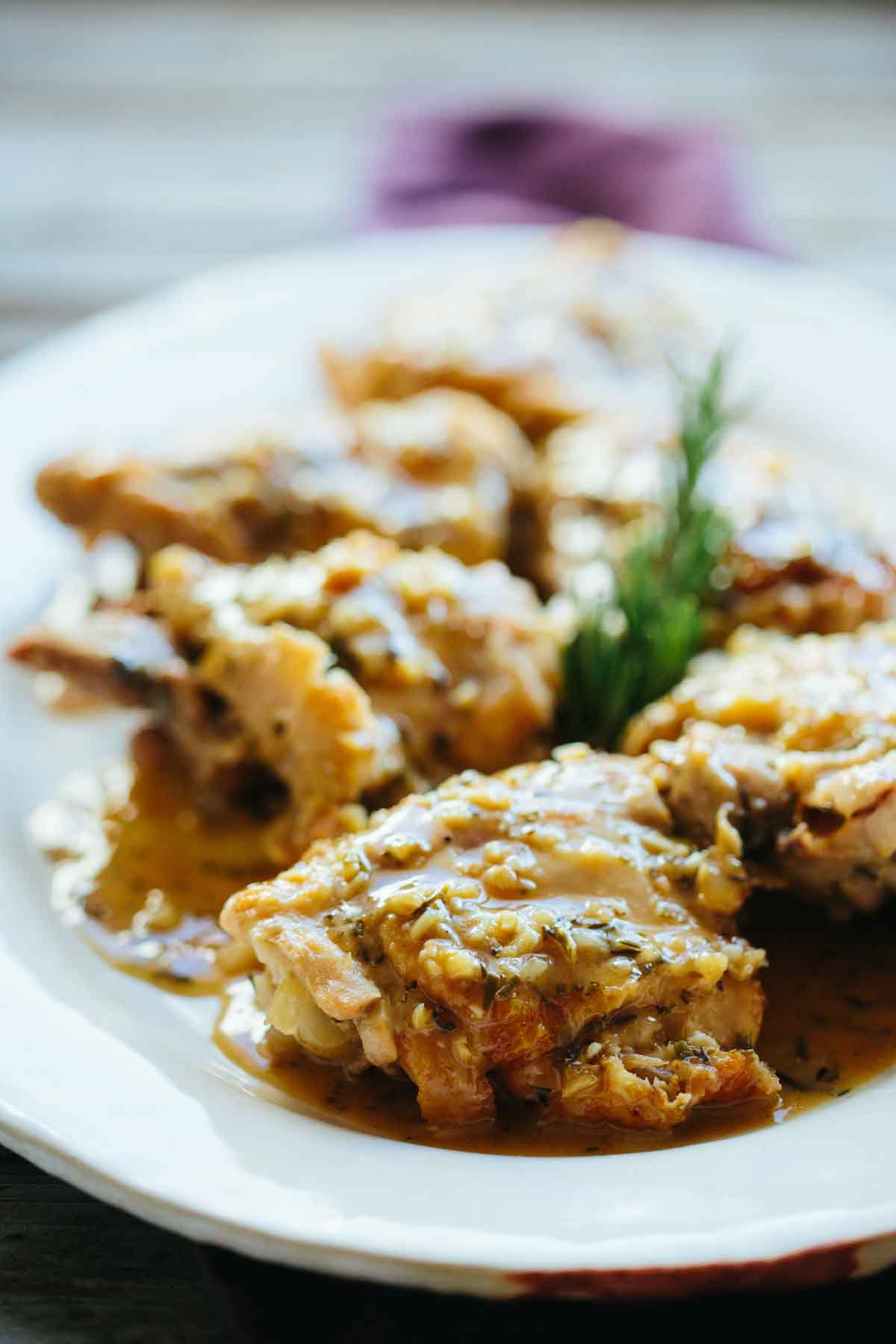 Close-up of tender chicken thighs on a white plate, glistening with a rich, herb-flecked sauce. A sprig of fresh rosemary garnishes the dish, highlighting the aromatic elements of this Roman-style cacciatore.