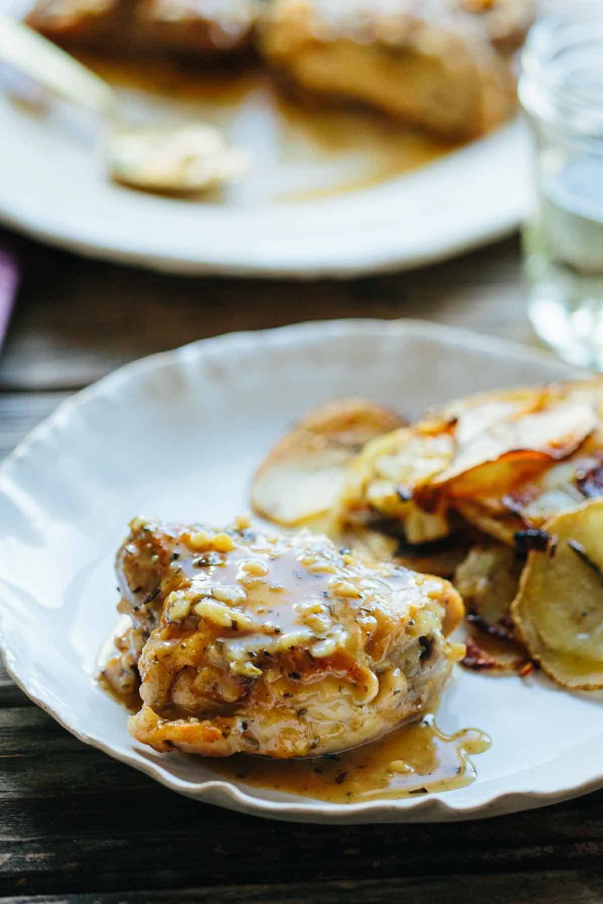 Close-up of a single piece of chicken cacciatore on a white plate with roasted potato slices visible in the background. The focus is on the moist chicken with its flavorful sauce and crispy exterior.