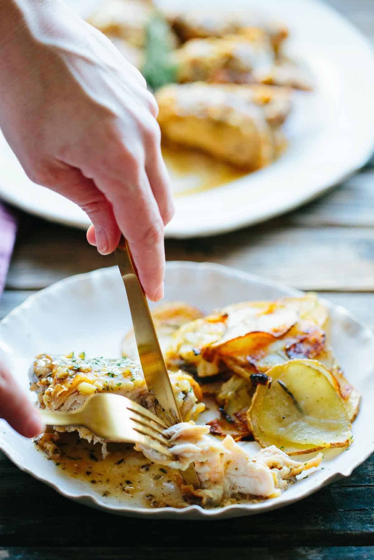 Close-up of a person cutting into a piece of the chicken cacciatore, showing the tender meat coming away easily. The second plate with roasted potatoes can be seen in soft focus in the background.